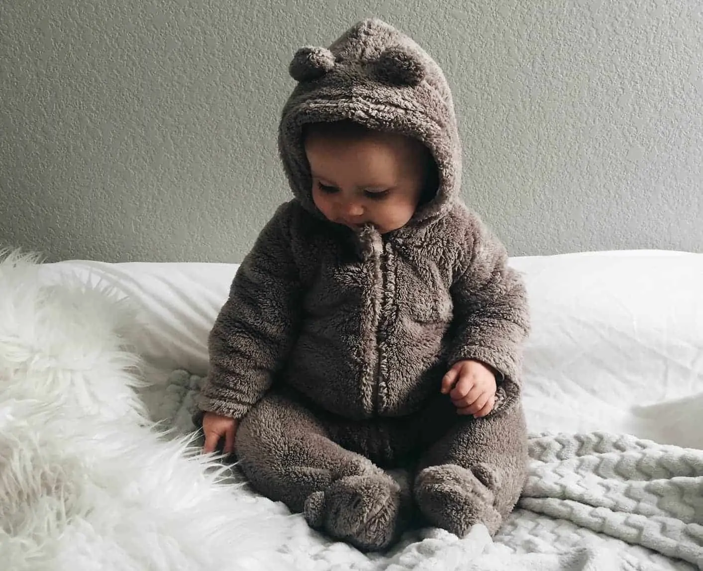 Baby in furry onesie sat on a cosy blanket